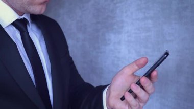 Siyah ceketli ve kravatlı bir iş adamı elinde telefonla e-postalarını kontrol ediyor ve ortaklarıyla bir toplantı planlıyor..