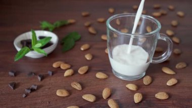 Badem sütü bir kaba akar. Etrafı badem, siyah çikolata ve nane yapraklarıyla çevrili..