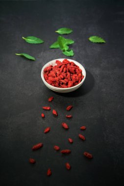 Siyah arka planda bir kasede Goji üzümleri. Nane yaprakları ve böğürtlenler.                               