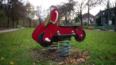 Sonbaharda çayırda kırmızı motosikletli bir bahar rockçısının yakınına. Arka planda ağaçlar var, ve sonbahar yaprakları çimenlere saçılmış..