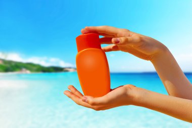 Kadın elleri güneş kremi şişesinden güneş kremi sürüyor.