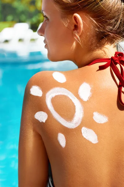 Νεαρή γυναίκα με το σχήμα του ήλιου στον ώμο κρατώντας αντηλιακή κρέμα μπουκάλι κοντά στην πισίνα — Φωτογραφία Αρχείου