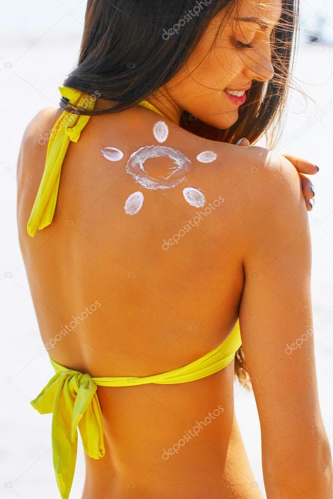 Portrait of gorgeous  woman smiling in bikini with the drawn sun on a shoulder at beach