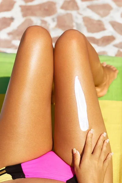 Fotografía recortada de una mujer joven que se aplica protector solar en las piernas mientras. Protector solar en las piernas . — Foto de Stock