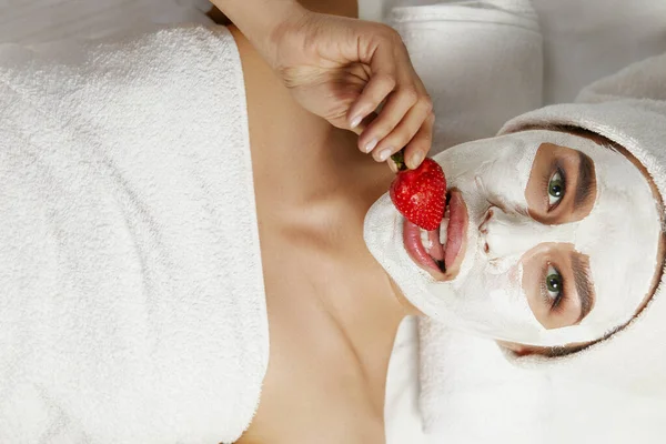顔に粘土マスクと手にイチゴを持つ美しい女性 顔の剥離マスク スキンケア — ストック写真