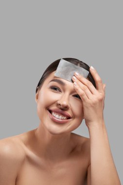 Yüz bakımı. Gülümseyen kadın, yüz yağlı kağıt kaplama portresi kullanıyor. Doğal makyajlı, yağ emici çarşaf ve güzellik ürünü kullanan güzel mutlu kız modelinin yakın çekimi.