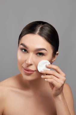 Beyaz yastıklı kadın temizleme yüzü. Makyaj beyazı pamuk pedi çıkartan güzel kız. Mutlu Gülümseyen Kadın kozmetik pedi ile yüz derisinden çıkıyor. Yüz Cildi Bakımı. 