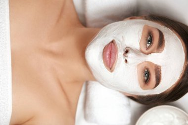 Yüzünde kil maske olan güzel bir kadının yakın plan portresi. Kadın tedavisinin yüz bakımı. Kozmetoloji. Cilt ve vücut bakımı.