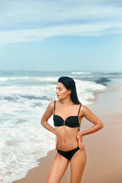 Portrait of young woman in black bikini on tropical beach looking at camera. Beautiful latin girl in swimwear with copy space. Sexy tanned body.