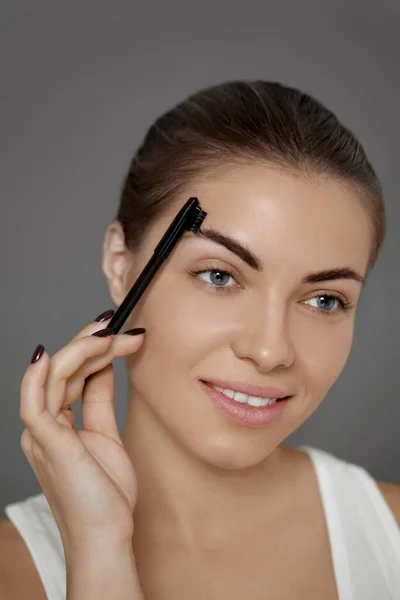 Eyebrows correction and contouring .  Beautiful woman shaping brows with comb.  Eyebrows and eyelashes close up