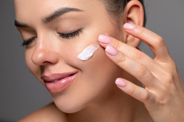 Cilt bakımı. Işıl ışıl ciltli genç bir kadının güzel portresi krem sürmeye başladı.