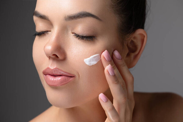 Уход за кожей. Красота крупным планом портрет молодой женщины с сияющей кожей наносит на кожу продукт. Гидратация. Мазок со сливками. Красивая модель с натуральным макияжем касается ее кожи
