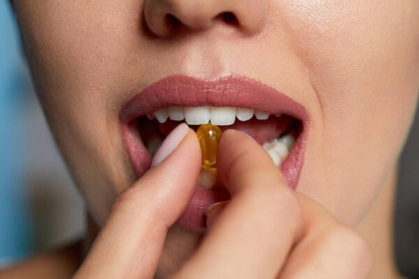 Женщина-кузнец держит в руках капсулу с маслом. Витамин и добавка. Портрет счастливой девушки, принимающей таблетку с маслом печени трески, Омега-3. Диетическое питание