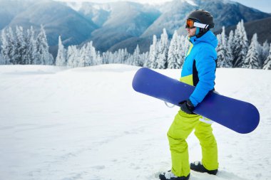 Kayak merkezindeki snowboardcu. Arka plandaki mavi gökyüzünde. Snowboard yapma. Kayak gözlüğü takıyor.