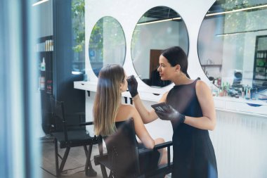 Bir güzellik uzmanı müşterisinin özelliklerini geliştirmeye odaklanırken aynı zamanda şık bir kuaföre gün ışığında makyaj yapar. Atmosfer sakin ve profesyonel..