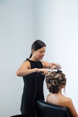 Bir stilist şık bir kuaför ortamındaki bir müşteri için saç kıvırıyor. Stilist, yaklaşan bir olayı parlak bir görünüm ile garantilemek için güzel bukleler yaratmaya odaklanıyor..