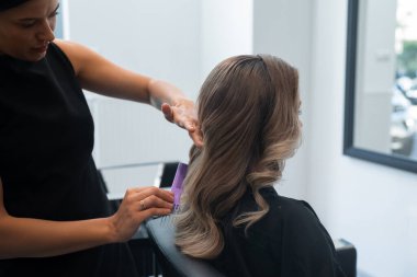 Bir stilist, müşterinin saçını öğleden sonra modern bir kuaförde dikkatlice şekillendirir. Detaylara ve kuaförlükteki becerilerine dikkat eder..