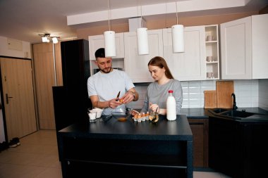 Açık renkli şık bir mutfakta, bir çift neşe içinde birlikte yemek pişirir. İçindekileri bir kasede karıştırıp hassas bir anı paylaşıyorlar ve sıcak bir atmosfer yaratıyorlar..