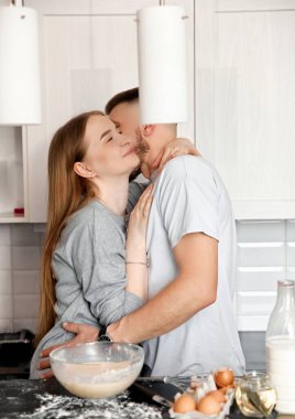 Bir çift, aşçılık malzemeleriyle dolu parlak bir mutfakta sevgi ve takım çalışması göstererek birlikte yemek hazırlıyor..