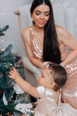 Genç bir anne ve kızı, Noel ağacını ışık ve süslerle süslerken neşeli bir anı paylaşıyorlar. Atmosfer sıcak ve şenlikli. Tatil için mükemmel..