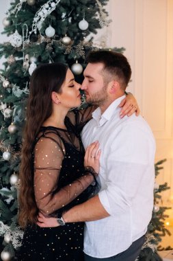 Bir çift, güzel süslenmiş bir Noel ağacının önünde sarılıp öpüşürken görülüyor. Sahne sıcaklık ve şefkat yayar, tatil sezonu için mükemmeldir..