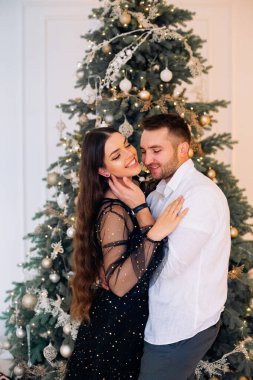 Bir çift, güzel süslenmiş bir Noel ağacının yanında dururken, sıcak ve şenlikli bir iç mekanda, altın süsler ve ışıklarla süslenmiş bir anı paylaşır..