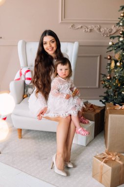 Bir anne ve küçük kızı, hediyelerle ve Noel ağacıyla çevrili rahat bir odada oturup, tatlı bir ziyafetin tadını çıkarıyor ve bayramları sevgi ve neşeyle kutluyorlar..