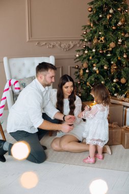 Ebeveynler kızlarıyla güzel vakit geçirmenin keyfini çıkarıyorlar. Etrafı hediyelerle ve sıcak bir ev atmosferindeki şenlikli süslemelerle çevrili bir Noel ağacının yanında. Tatil sezonunun keyfini çıkarıyorlar..