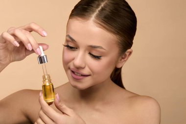 Stüdyodaki kadın deri sağlığını geliştirmek için cilt serumu kullanıyor. Şişeye odaklanıyor ve yüz bakımına yağlarla hazırlanıyor. Ortam aydınlık ve sıcak..