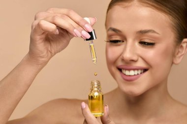 Kadın bir şişe serumun üzerinde bir damlatıcıyı tutuyor, cilt ürününü sürmeye hazırlanıyor yüz parlaklığını arttırmak ve stüdyo ortamında sağlıklı cildini korumak için..