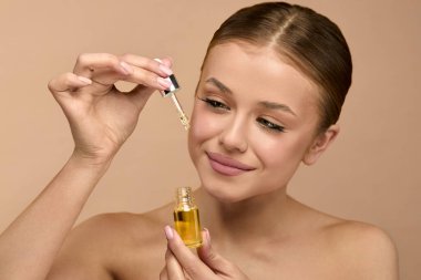 Kadın stüdyo ortamında serumu yüzüne sürüyor. Derisinin görünüşünü ve sağlığını iyileştirmek için cilt bakımına odaklanıyor.