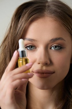 Çarpıcı mavi gözlü bir kadın kameraya bir şişe serum tutarak gün içinde sıcak ve davetkar bir şekilde parlayan derisini sergiliyor..