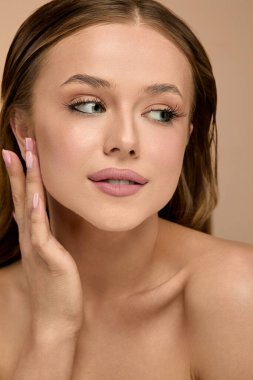 Kadın eliyle yanağına dokunurken yumuşak tenini gösteriyor. Bir stüdyo ortamında bakışları kameradan uzaklaşırken derin düşüncelere dalıyor..