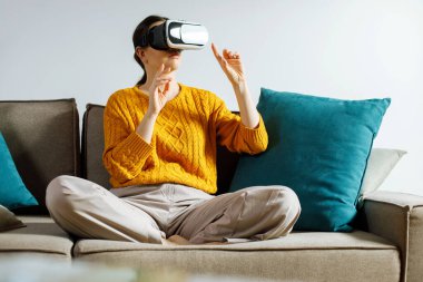 Bireyler oturma odasındaki bir kanepede otururken sanal gerçeklik kulaklığı takarlar. Rahat kıyafetler giyiliyor ve atmosfer rahatlamış görünüyor..