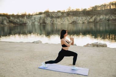 Bir kadın şafak vakti dingin bir gölün kenarındaki yoga minderine atlıyor. Kayalık kayalıklar yumuşak ışığı yansıtıyor, barışçıl bir çalışma ortamı yaratıyor..