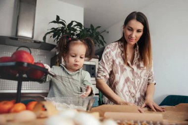 Bir anne ve küçük kızı mutfakta yan yana çalışıyorlar. Anne kurabiye için şekil kesmeye hazırlanırken çocuk hamur karıştırır. Sıcak, güneşli bir öğleden sonra..
