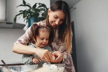 Bir anne ve kız mutfakta birlikte çalışıp, pişirme etkinliği için yumurta kırıyorlar. Birlikte iyi vakit geçirirken gülümseme paylaşıyorlar..