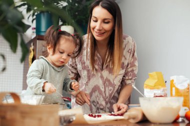 Bir anne ve küçük çocuğu mutfakta birlikte hamuru yuvarlıyor ve tatlı olarak bir şeyler ekliyorlar. Onlar bu işle meşguller ve hafta sonları eğlenceli bir anı paylaşıyorlar..