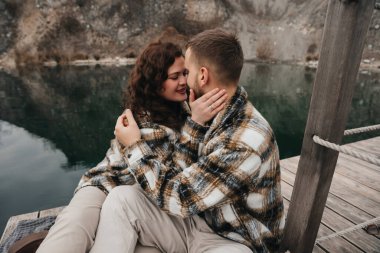 Serin bir günde, aynı kıyafetlerle aşkı kutlarken iki kişi limanda romantik bir anı paylaşıyor..