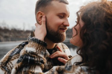 İki insan, sevgililer gününde birbirlerine sevgi ve sevgi göstererek su kenarında dururlar. Manzaralı bir arkaplanla..