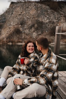 Göl kenarındaki ahşap bir rıhtımda iki kişi oturuyor. Sıcak içecekler içerken birbirlerine gülümserler. Serin bir gün..