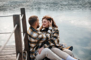 Erkek ve kadın, bir su kütlesinin yanındaki ahşap rıhtımda yan yana oturuyorlar. Sessiz bir anın tadını çıkarıyor ve birbirlerine gülümsüyorlar..
