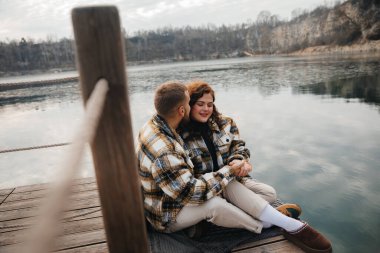İki insan sakin bir gölün kenarında otururlar, Sevgililer Günü 'nde sıcak ceketler giyerek sevgi dolu bir anı paylaşırlar..