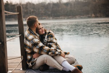 Bir adam ve bir kadın suyun kenarında oturur, birbirlerine sarılırlar, Sevgililer gününde manzaralı bir gölün yanında bir anı paylaşırlar..