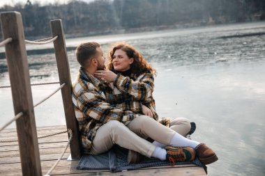 Bir adam ve bir kadın göl kenarındaki rıhtımda birlikte oturuyorlar. Sıcak giysiler içinde gülümsemelerini paylaşırken yakın bir anın tadını çıkarırlar..