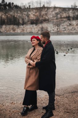 Sevgililer Günü 'nde bir erkek ve bir kadın göl kenarında, kış kıyafetlerini giyerken romantik bir anı paylaşıyorlar..