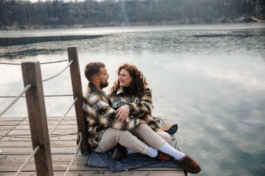 Bir adam ve bir kadın serin bir günde suyun kenarında yan yana otururlar. Gülümsüyorlar ve sevgi ve bağlantı anlarını paylaşıyorlar..