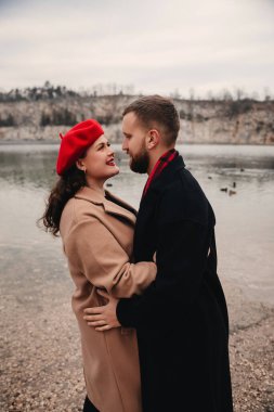 Bir adam ve bir kadın gölün kenarında durur, sıcak bir şekilde giyinip, sevgi dolu bakışlarını paylaşırlar..