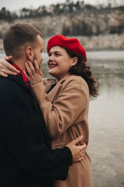 Sevgililer Günü 'nde aşklarını kutlarken bir erkek ve bir kadın kışın bir su kütlesinin yanında gülüp kucaklaşıyorlar..