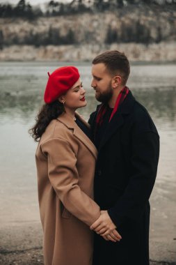 İki insan, Sevgililer Günü sahnesinde suyun kenarında el ele tutuşup birbirlerine sevgiyle bakar..